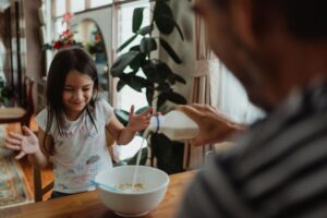 A father pouring milk for his daughter during breakfast in a cozy kitchen.