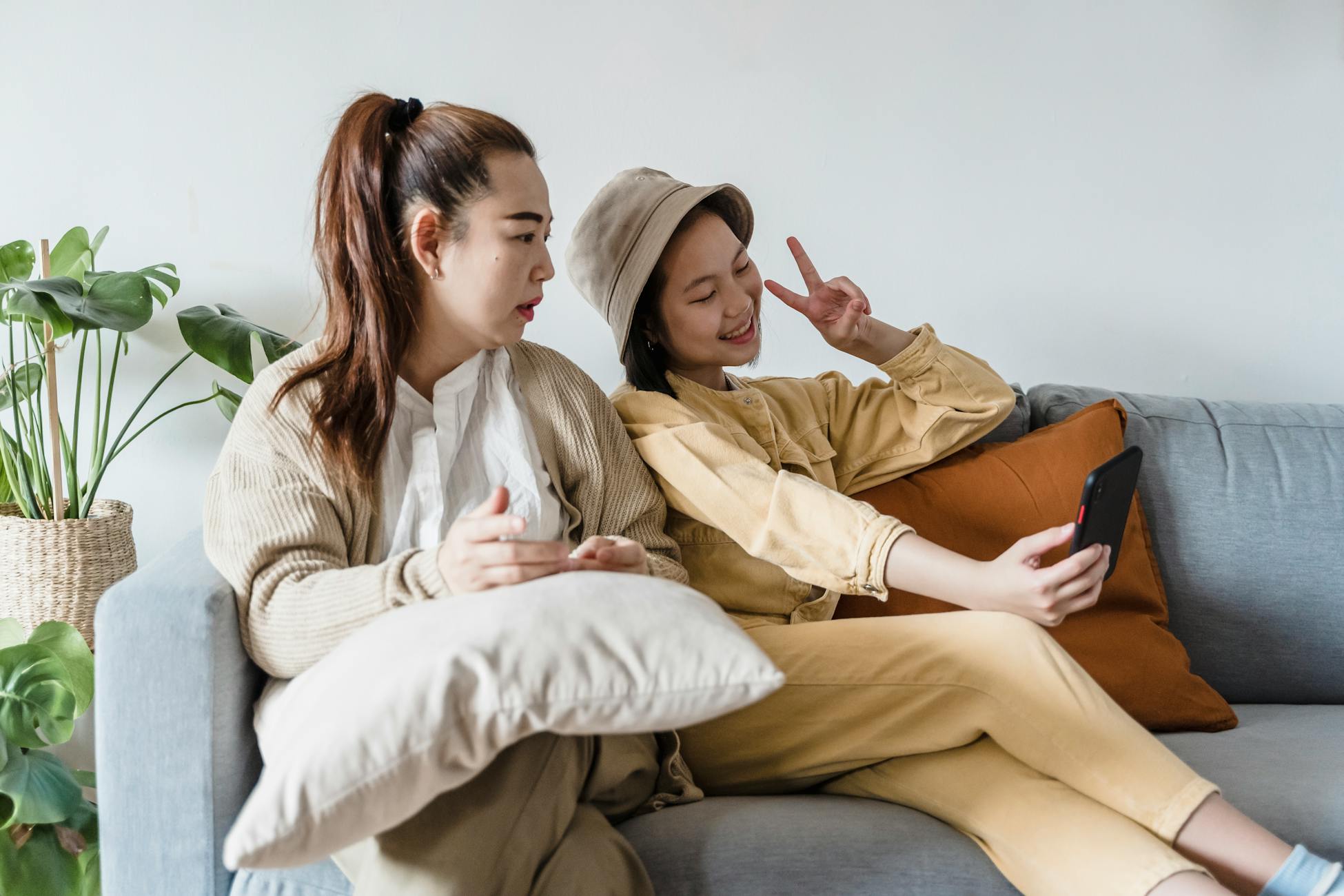A mother and daughter sit on a couch at home, capturing a selfie together.