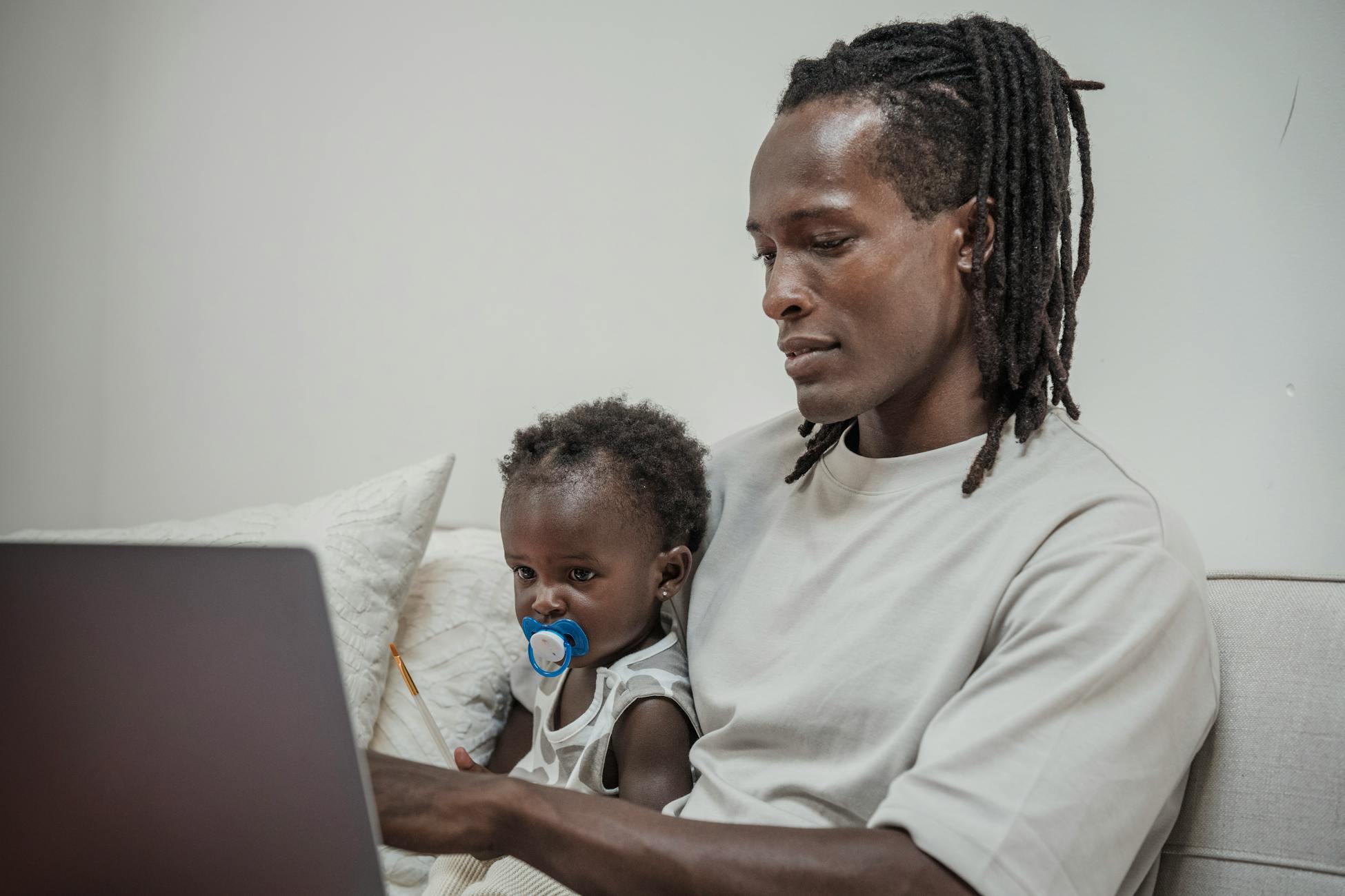 A father bonding with his baby daughter while using a laptop together on the sofa.