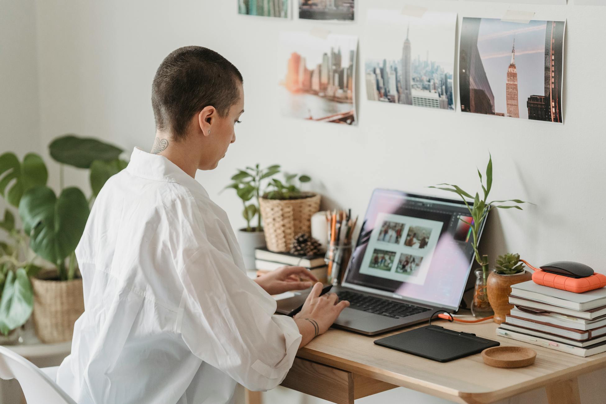 A woman focuses on photo editing at her stylish home desk with laptop and decor.