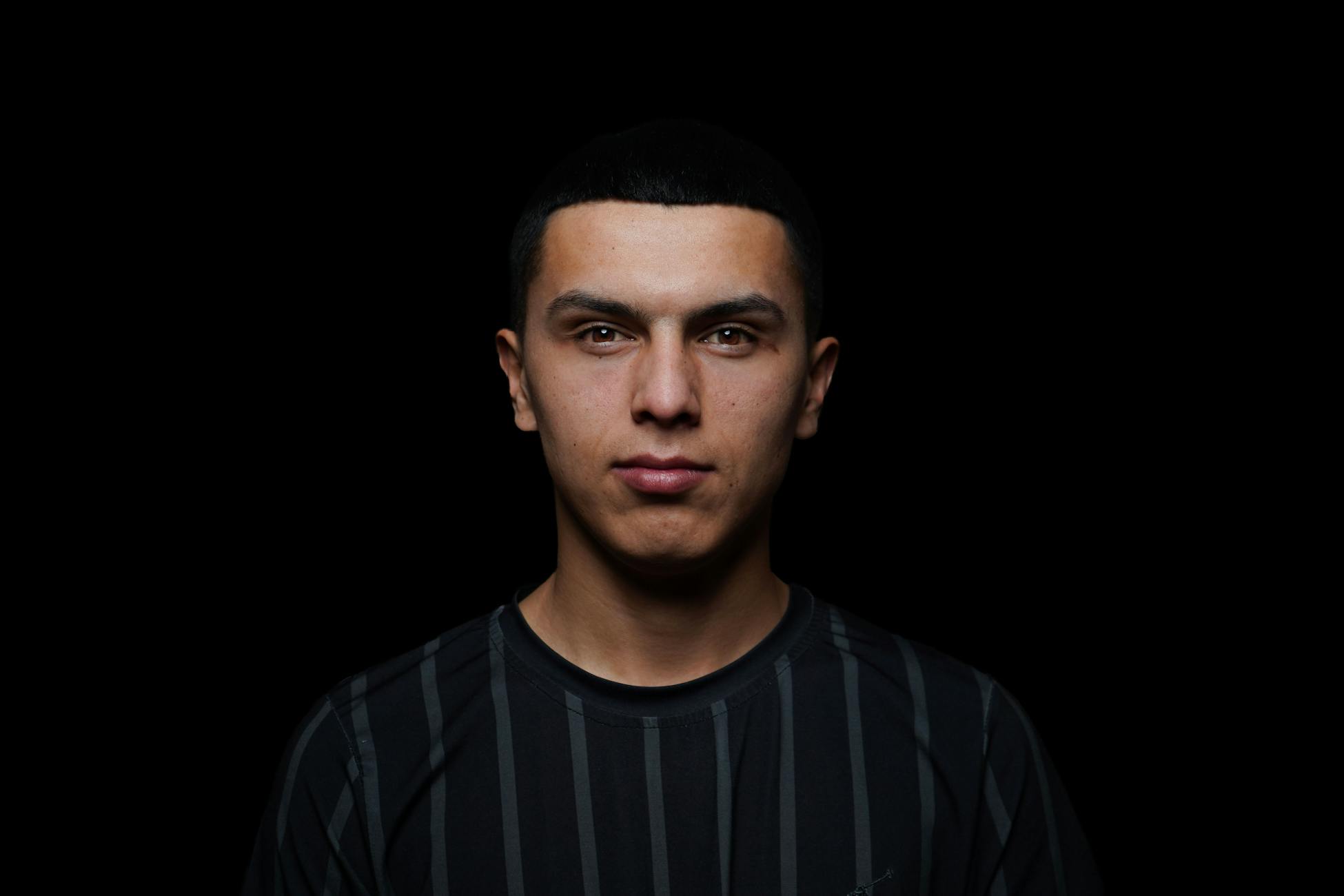 Studio portrait of a young man with a serious expression on a black background.