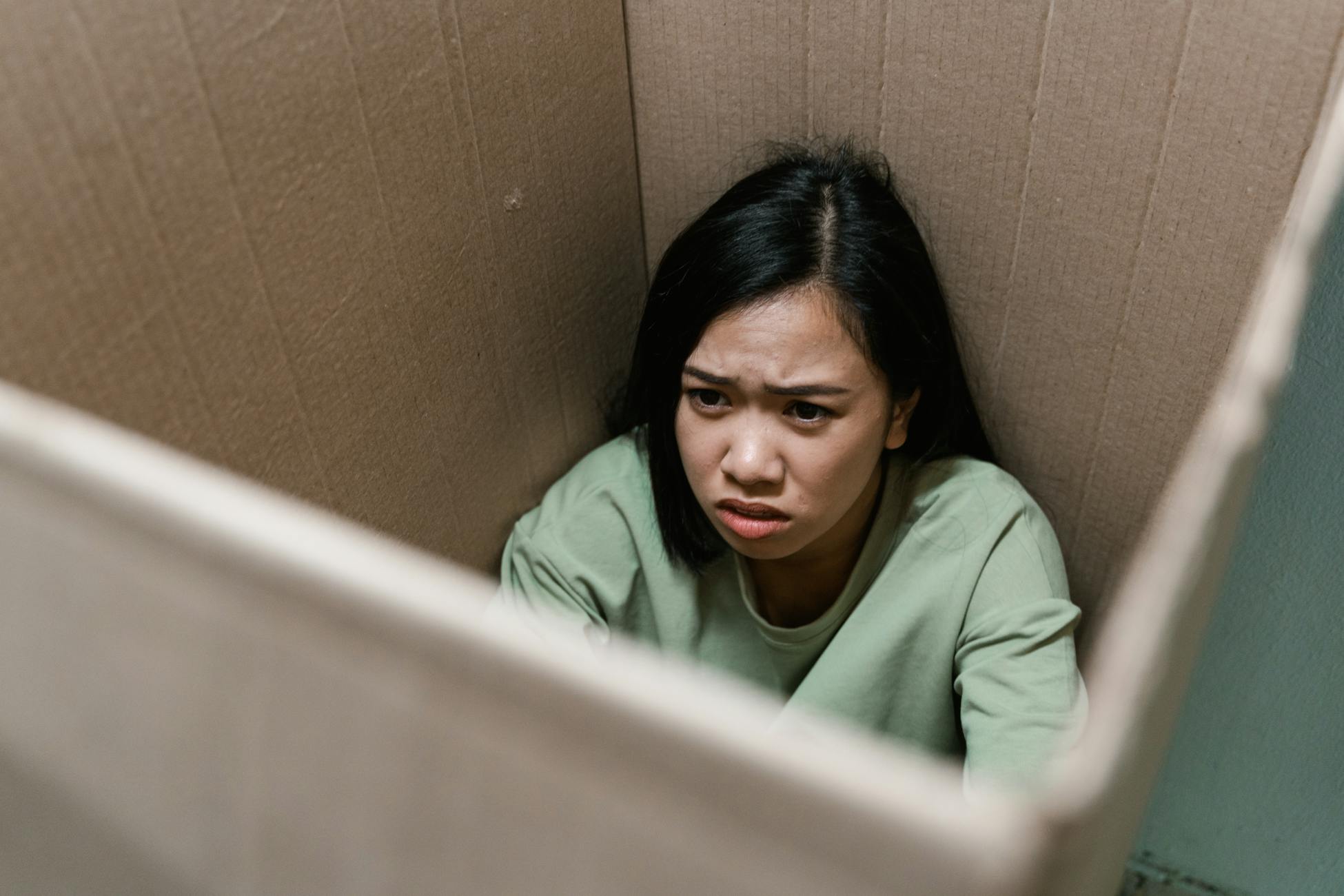 A woman inside a cardboard box showing a distressed expression, symbolizing anxiety or claustrophobia.