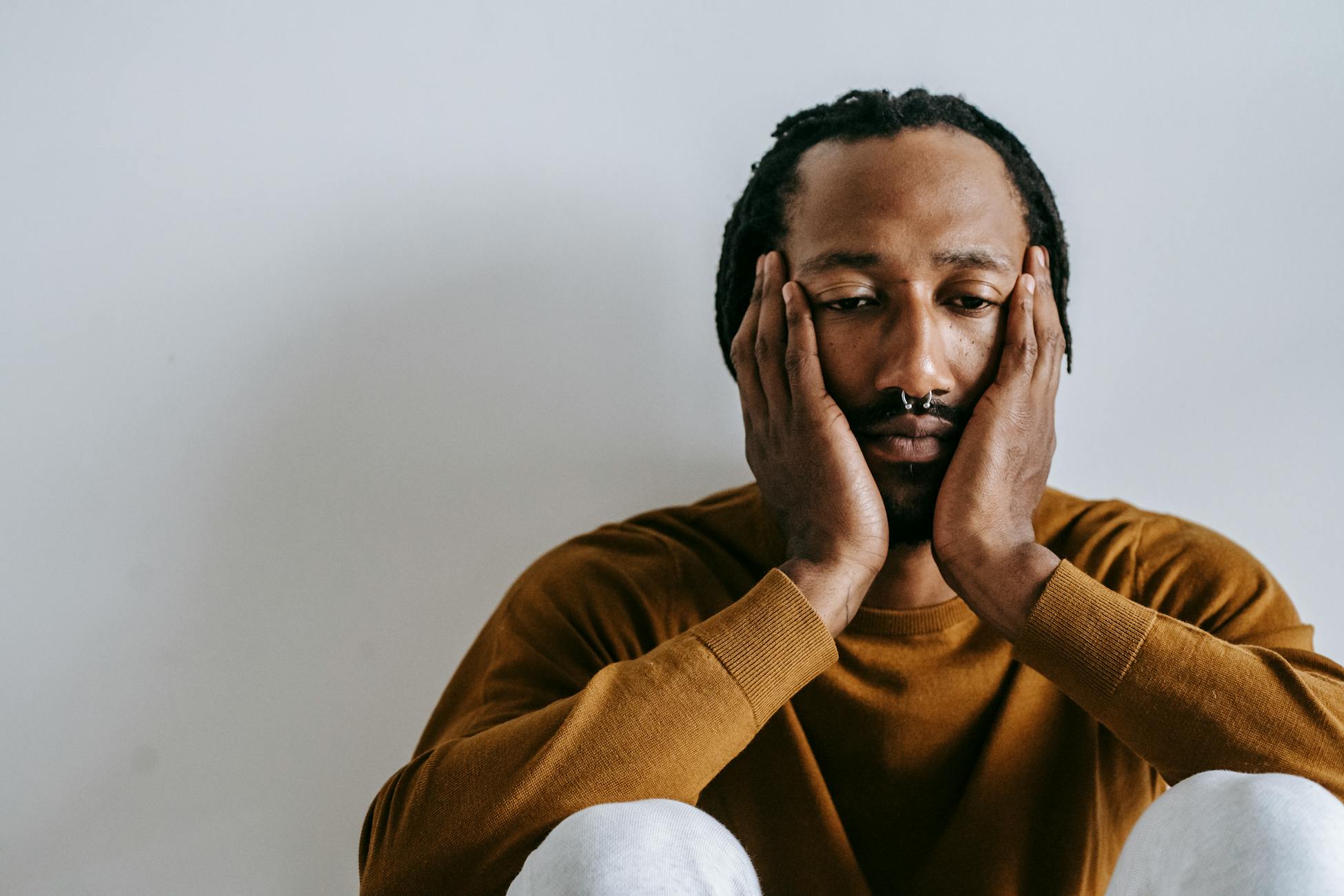 Portrait of a thoughtful man, hands on face, in a light setting.