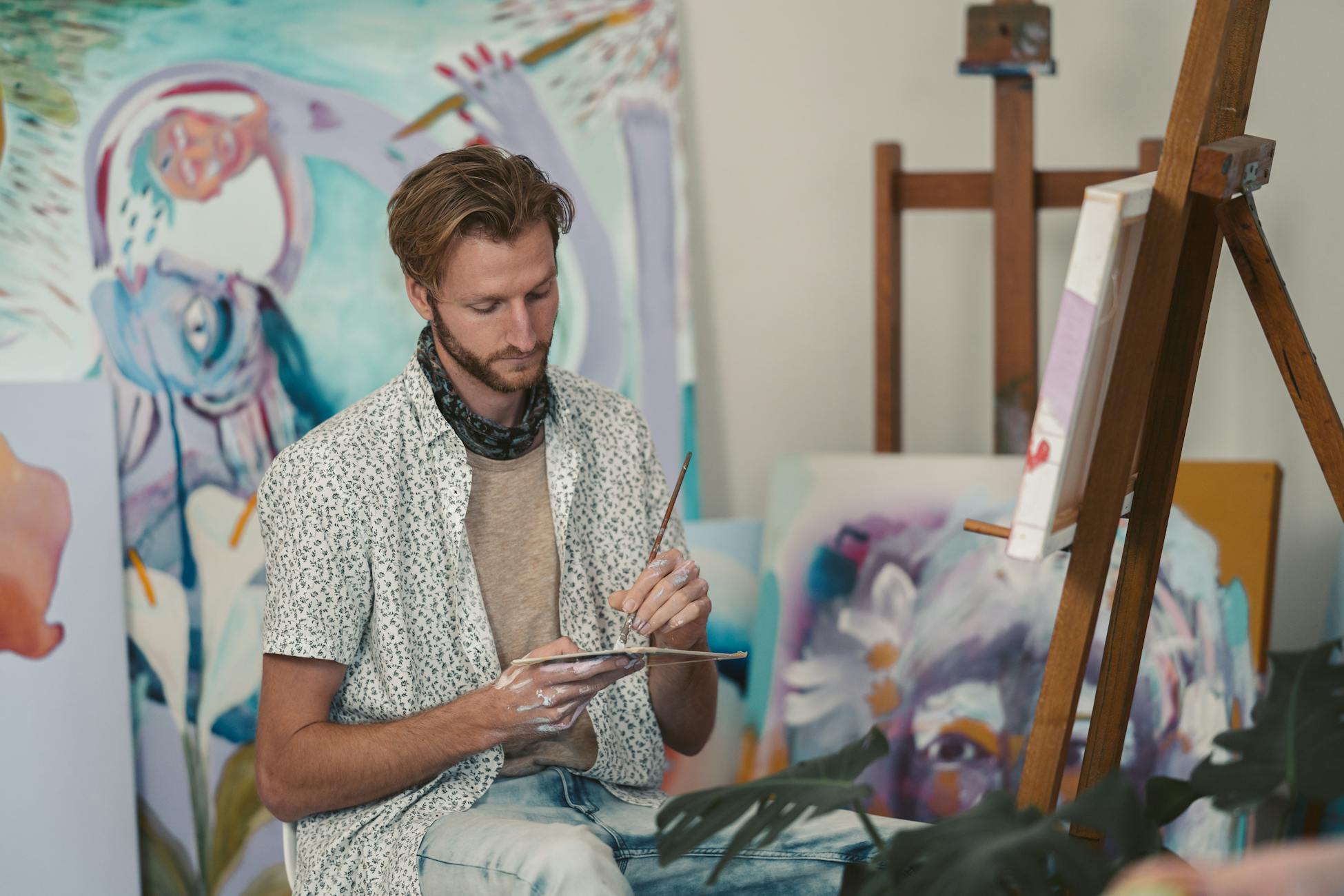 Male artist focused on painting in a creative art studio with abstract canvases.