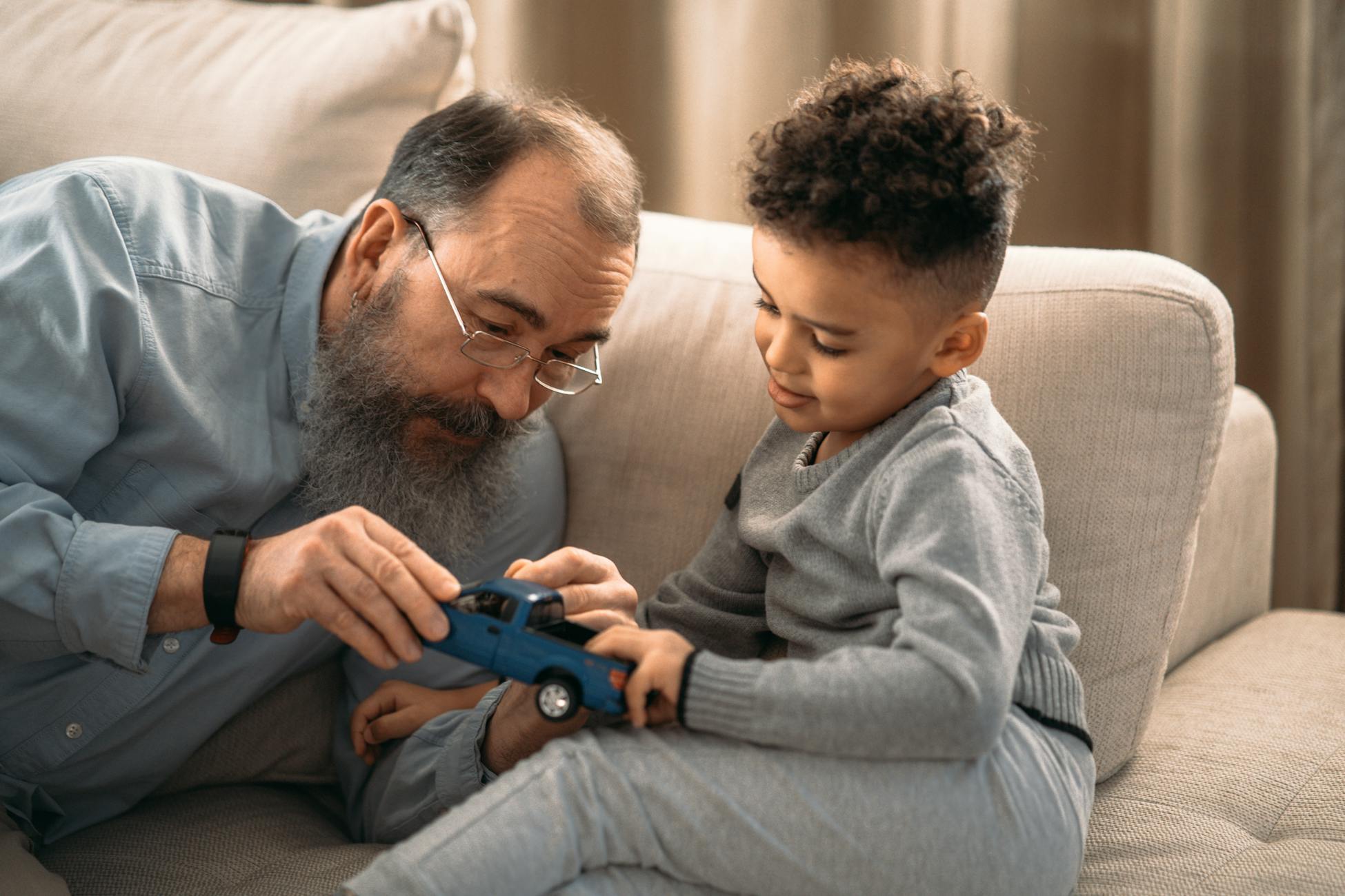 An elderly man and young boy bond while playing with a toy car indoors, showcasing family love.