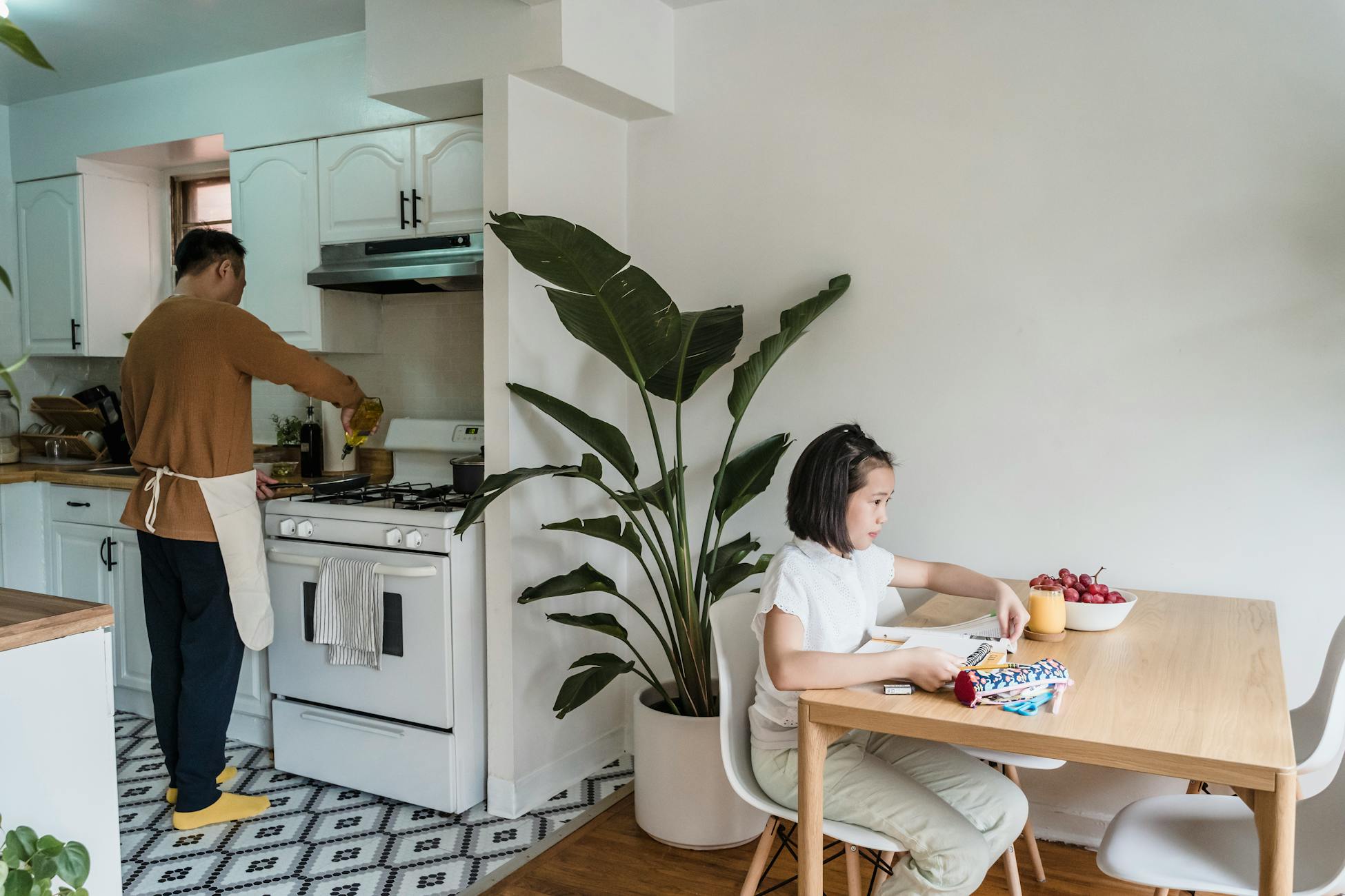 Father cooking while daughter studies in a cozy kitchen setting.