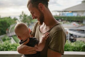 A bearded father holds his baby, sharing a tender moment outdoors.