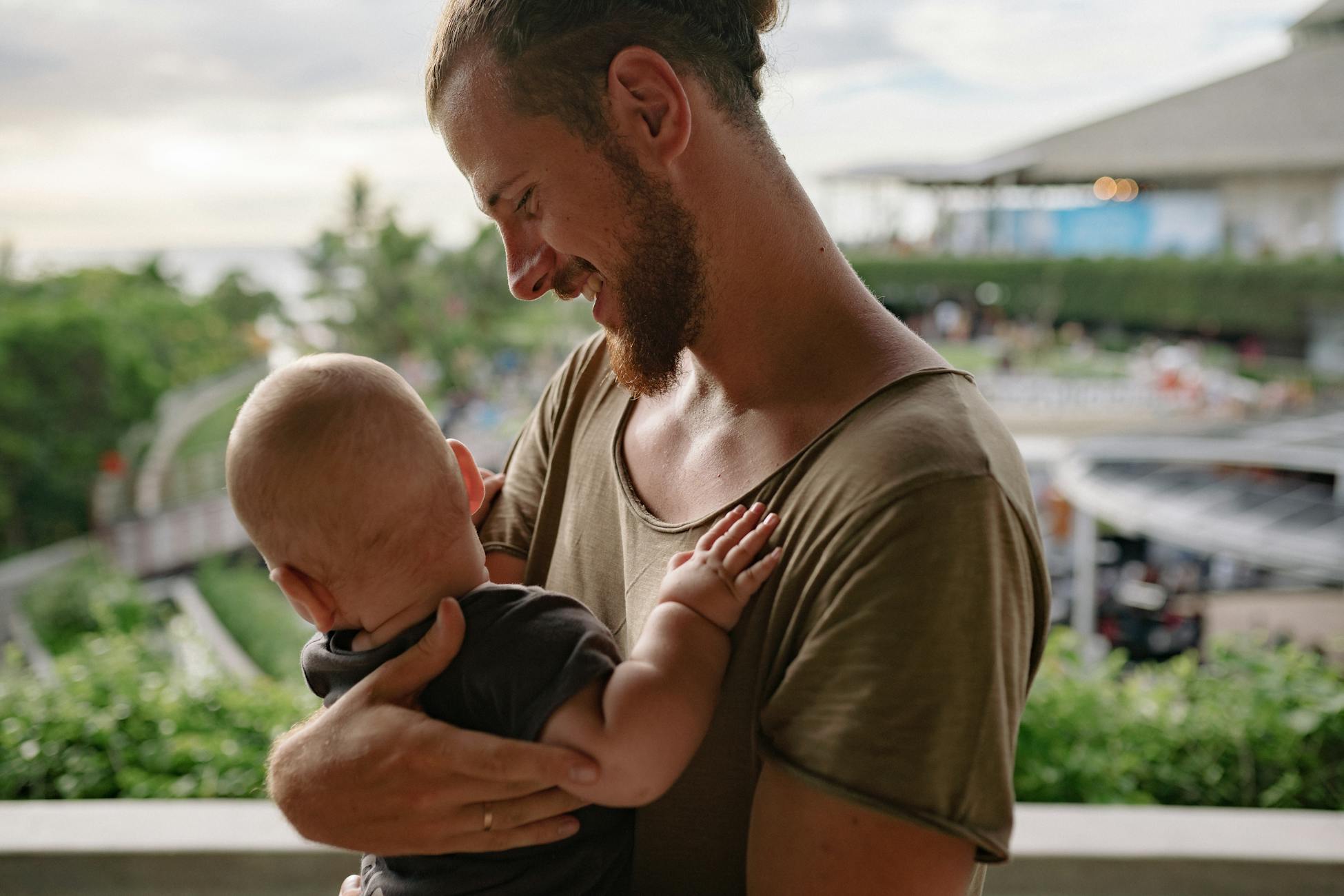 A bearded father holds his baby, sharing a tender moment outdoors.