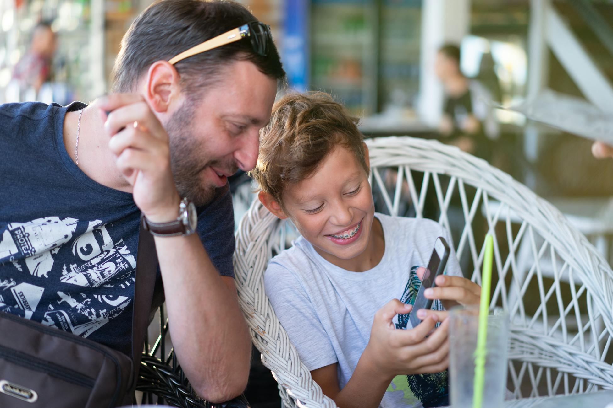 Father and son bonding over a smartphone, sharing a joyful moment in a cozy cafe.
