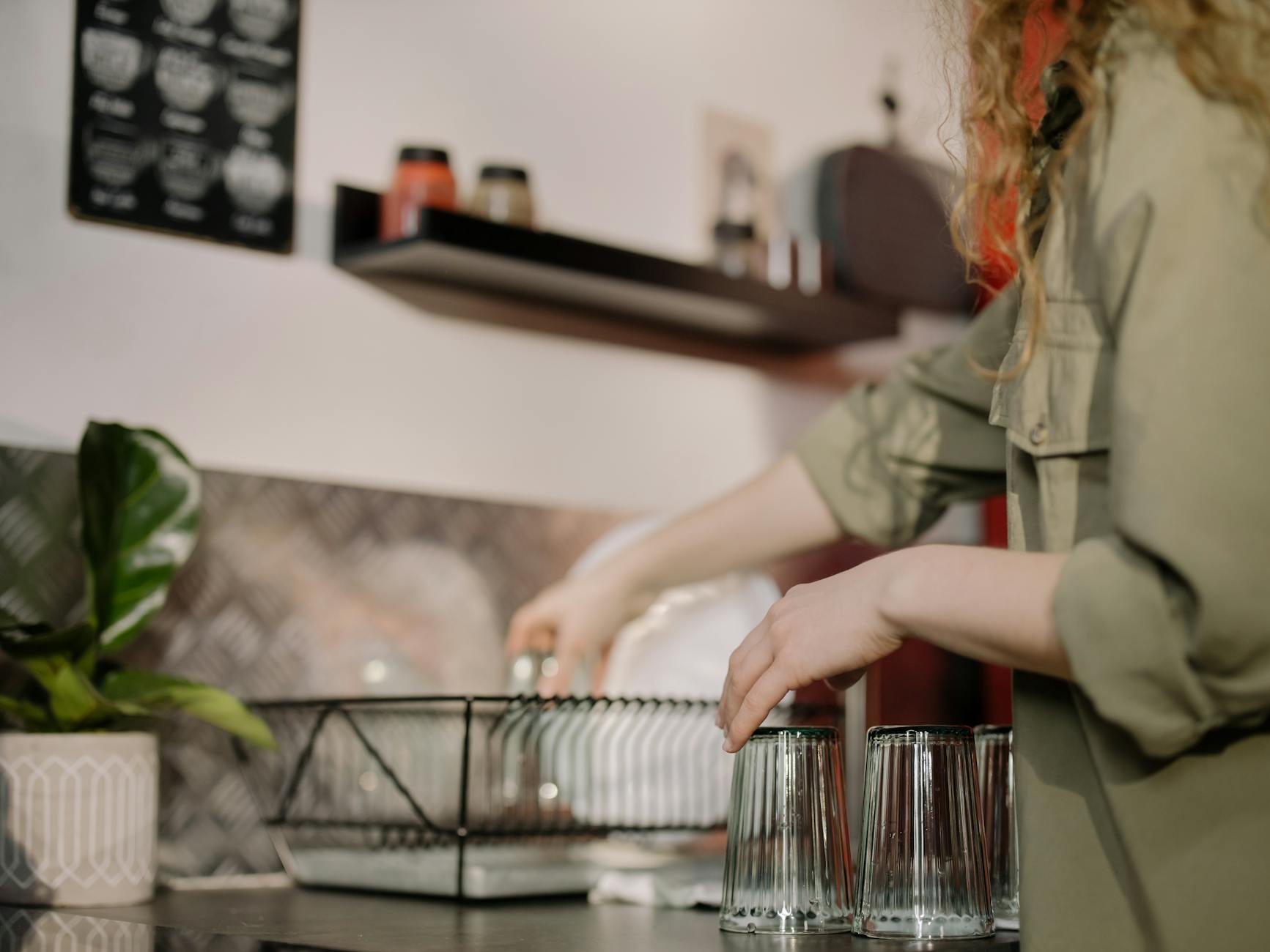 A person arranging clean glasses on a kitchen counter. Cozy home kitchen scene.