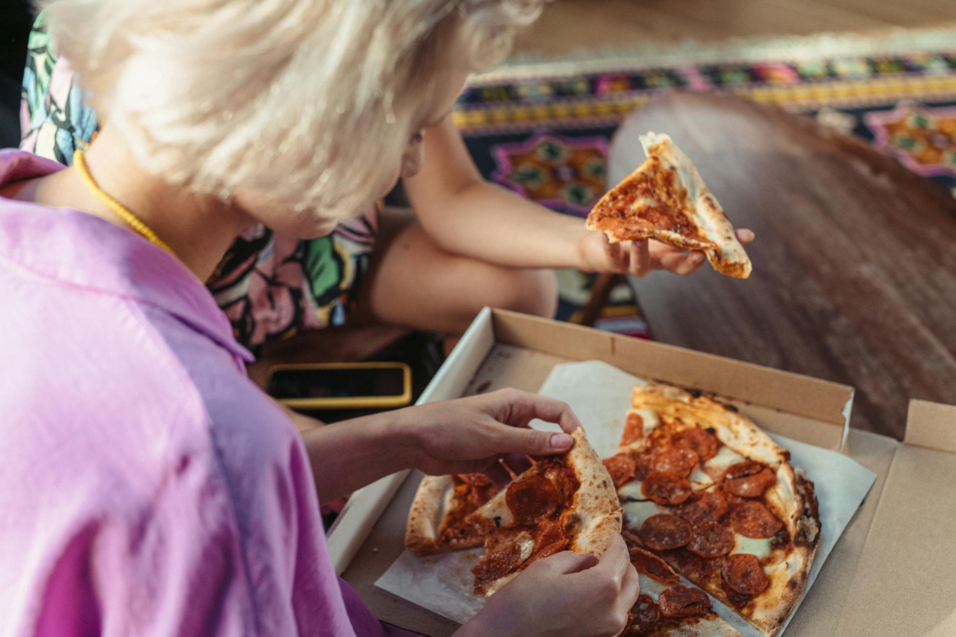 Two friends enjoying pepperoni pizza indoors, sitting together for a casual meal.