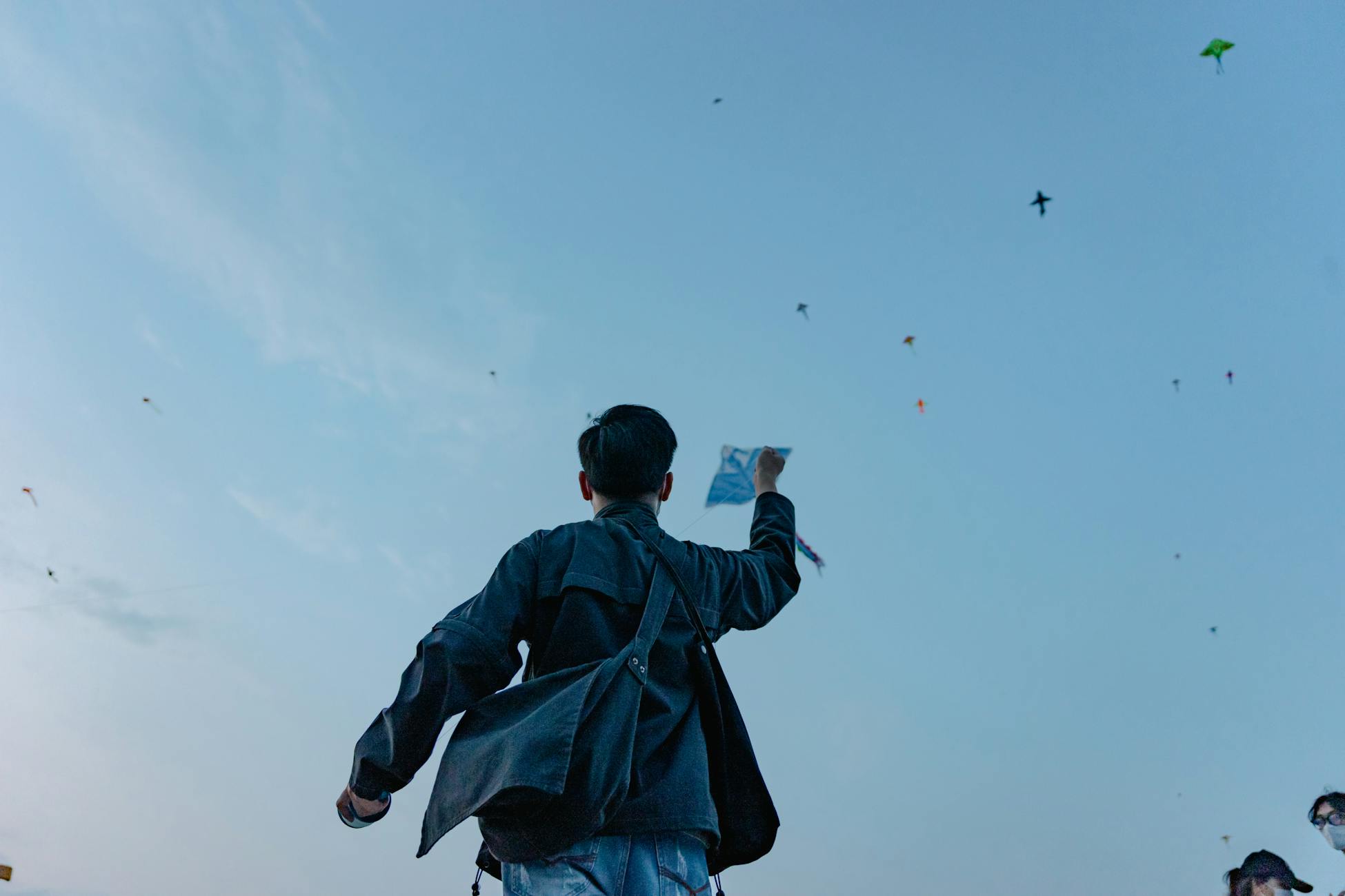 A man flying a kite among many others in a clear blue sky during a festival.