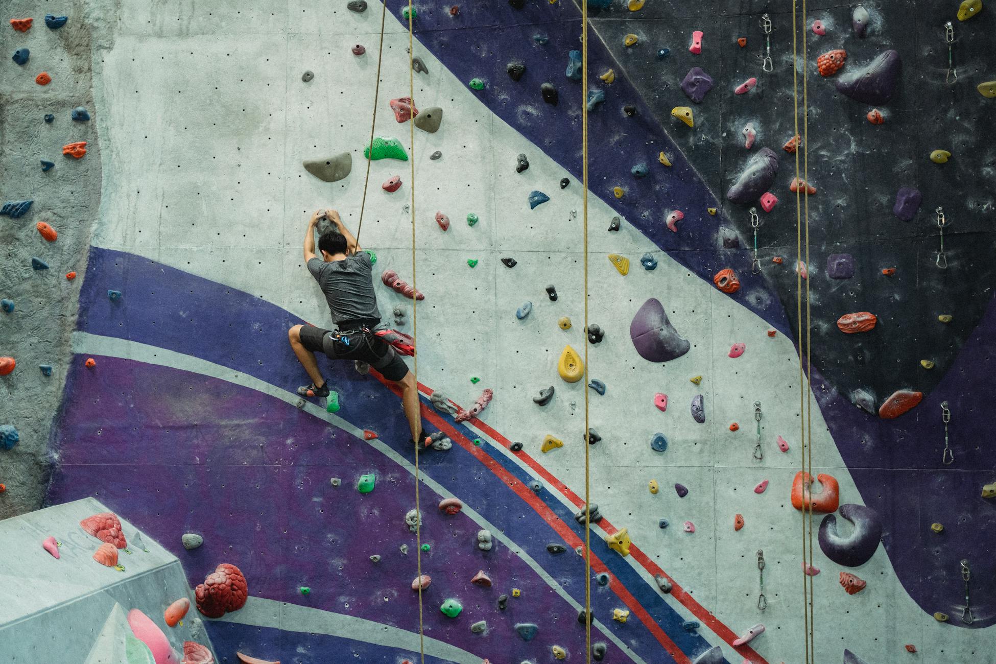 Full length of anonymous male mountaineer with equipment clambering wall during workout in gym
