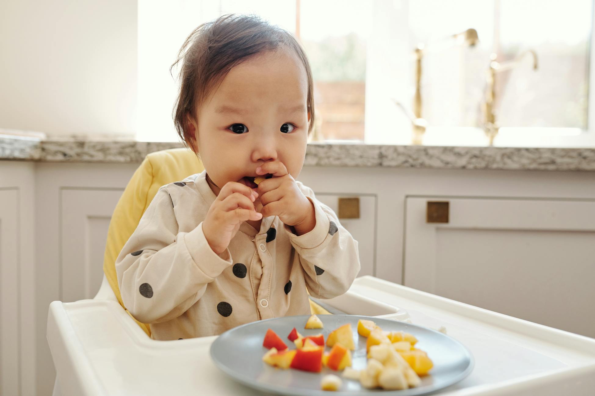 Adorable toddler enjoying fresh fruit pieces in a high chair at home.