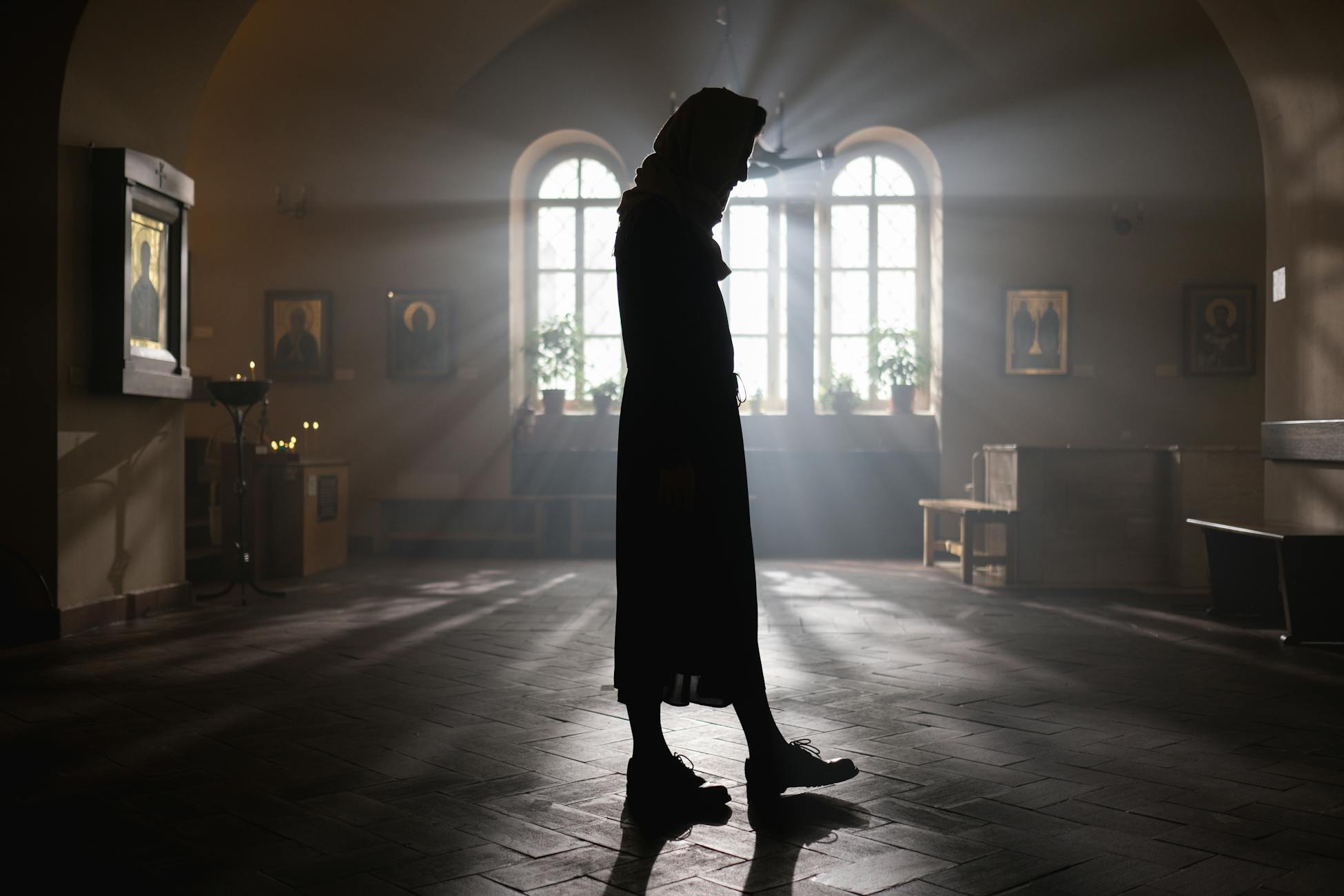 A woman stands silhouetted in an atmospheric orthodox church, light streaming through windows.