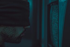 A close-up of a blindfolded man facing a static television screen in a dark room.