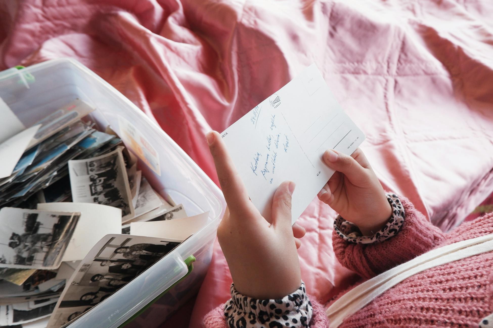 Close-up of a woman holding a postcard, exploring memories from a photo box.