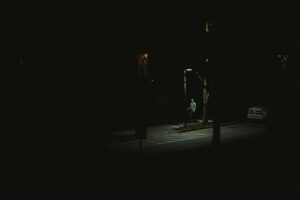 A lone person walking under a streetlight on a dark city street at night.