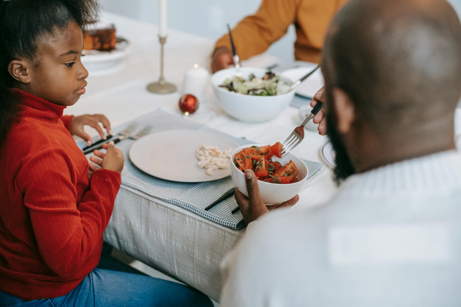 Thoughtful African American girl expecting salad in plate with forks placed on festive table