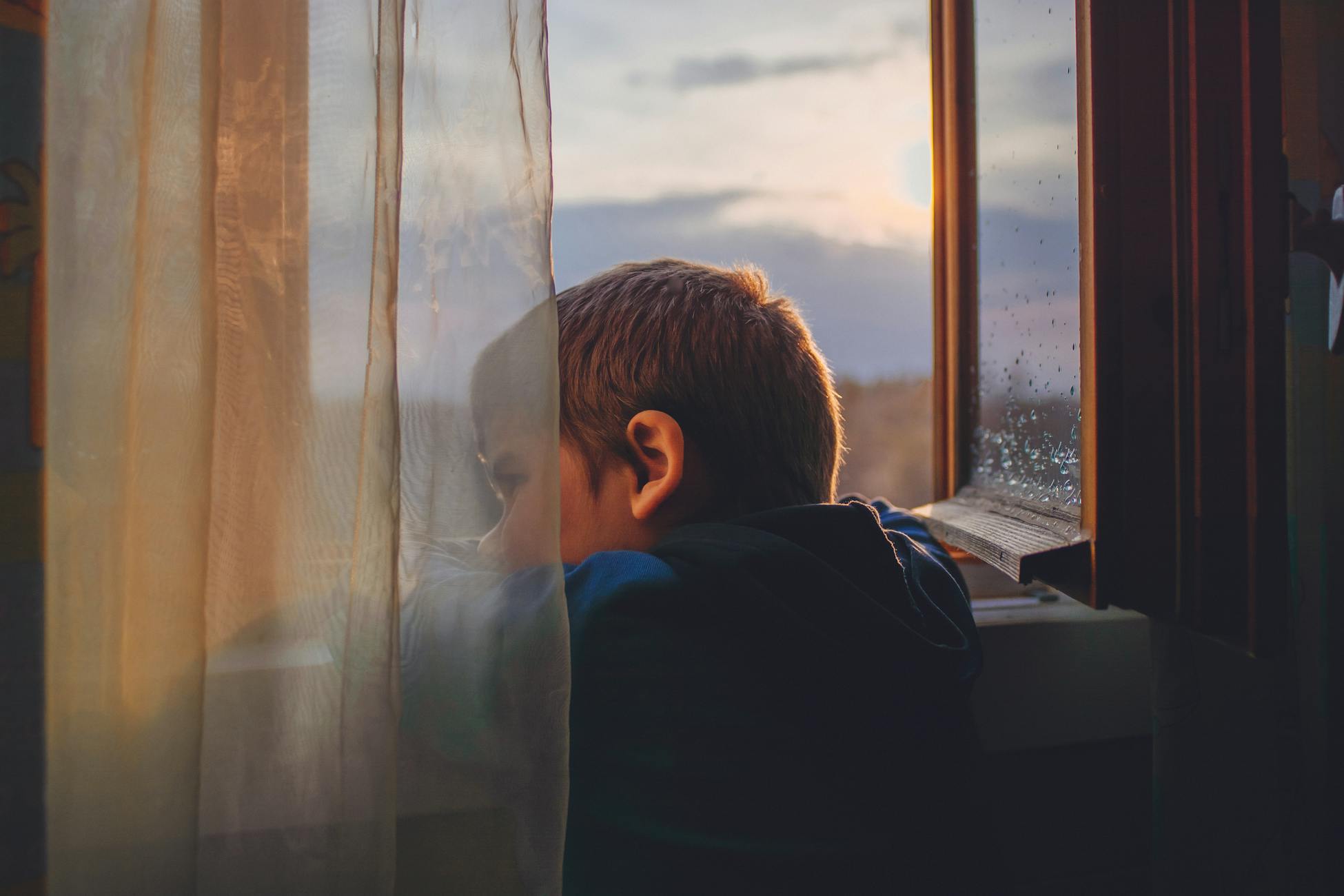 Young boy looking through window, captured during a tranquil sunrise indoors.