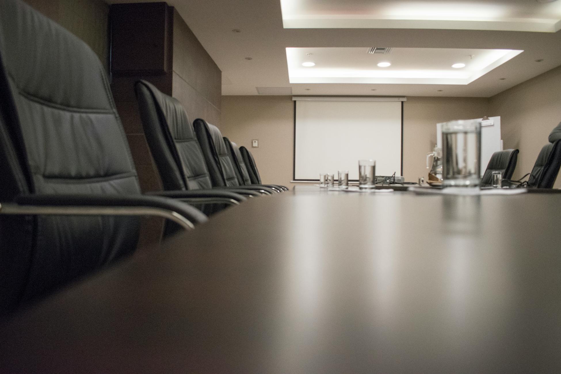 Empty conference room with black chairs, projector, and glasses on table. Ideal for business meetings.