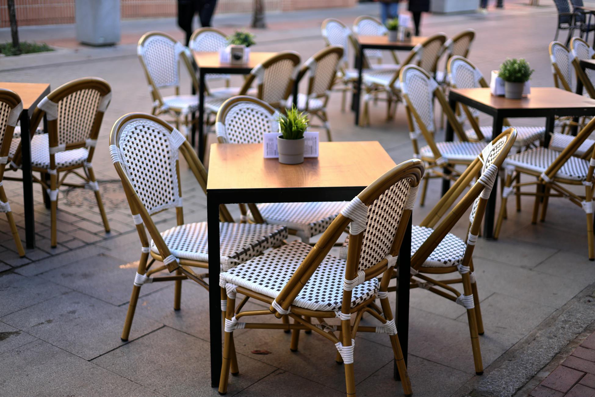 Empty outdoor cafe setting with wicker chairs and wooden tables in a lively Spanish street.