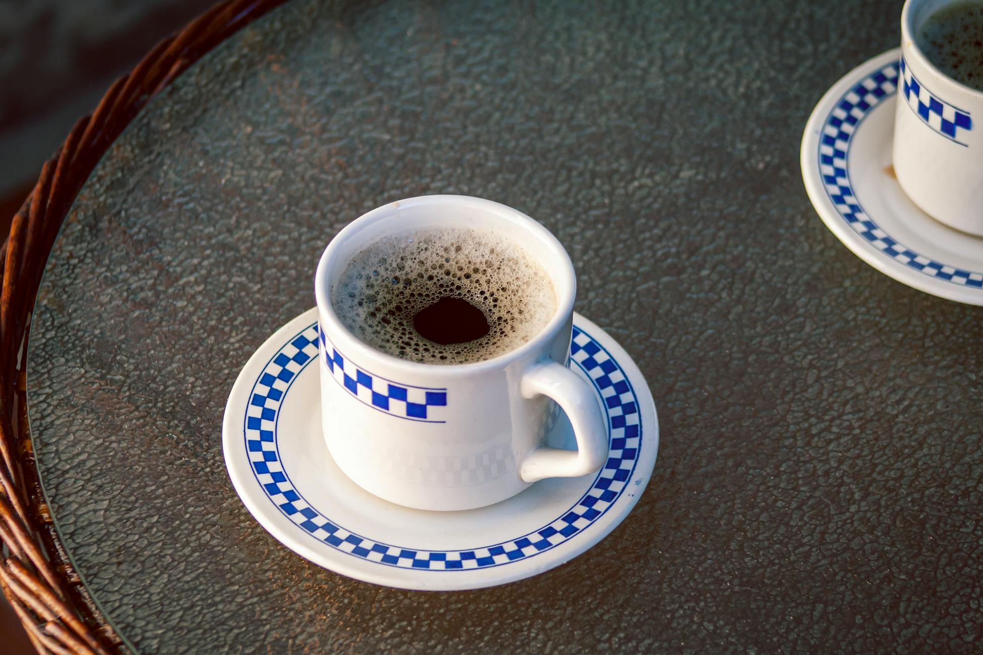 Artistic shot of coffee cups with blue checkered pattern on a glass table.