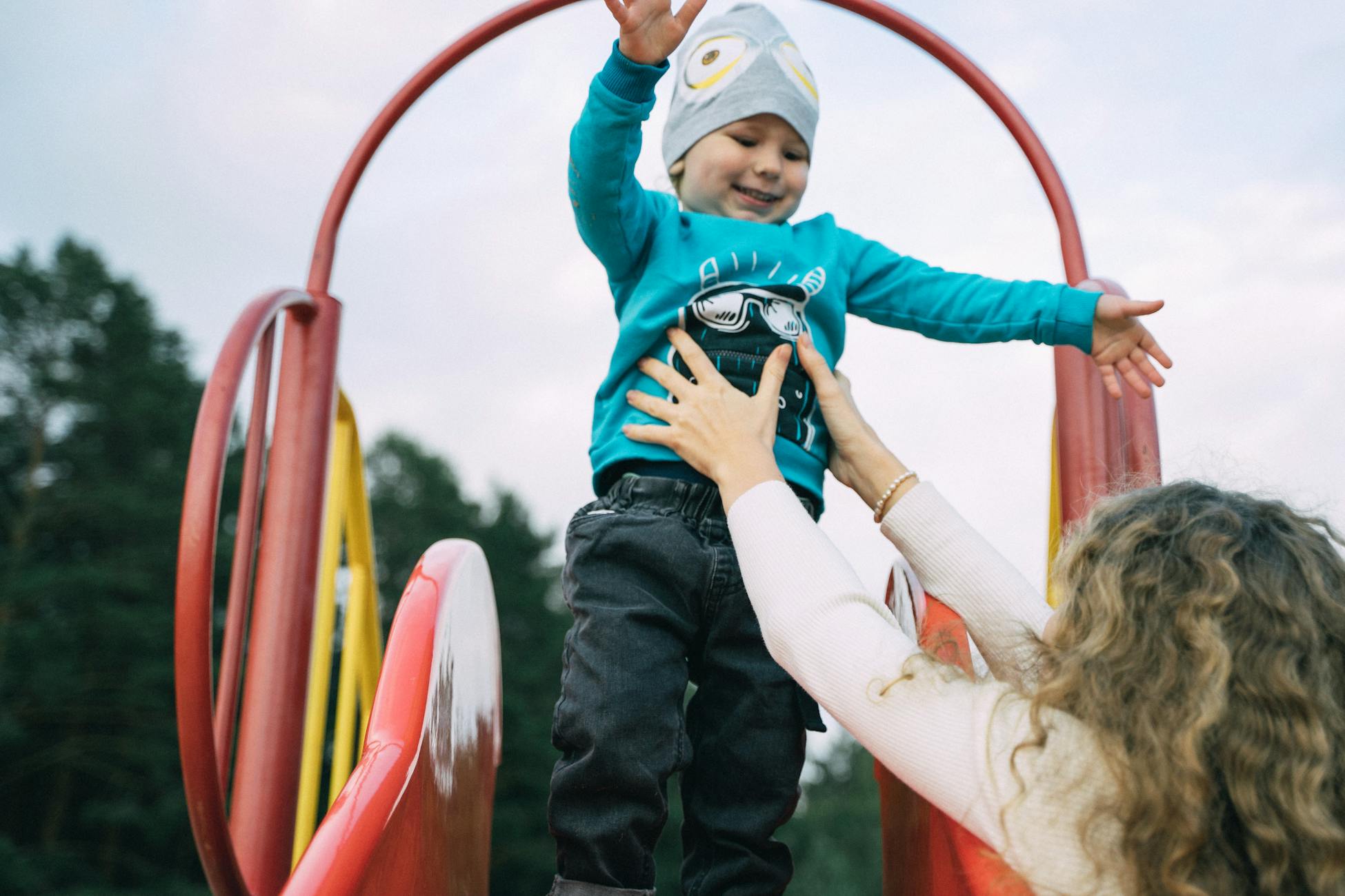 A joyful moment of a mother catching her child at the top of a playground slide.