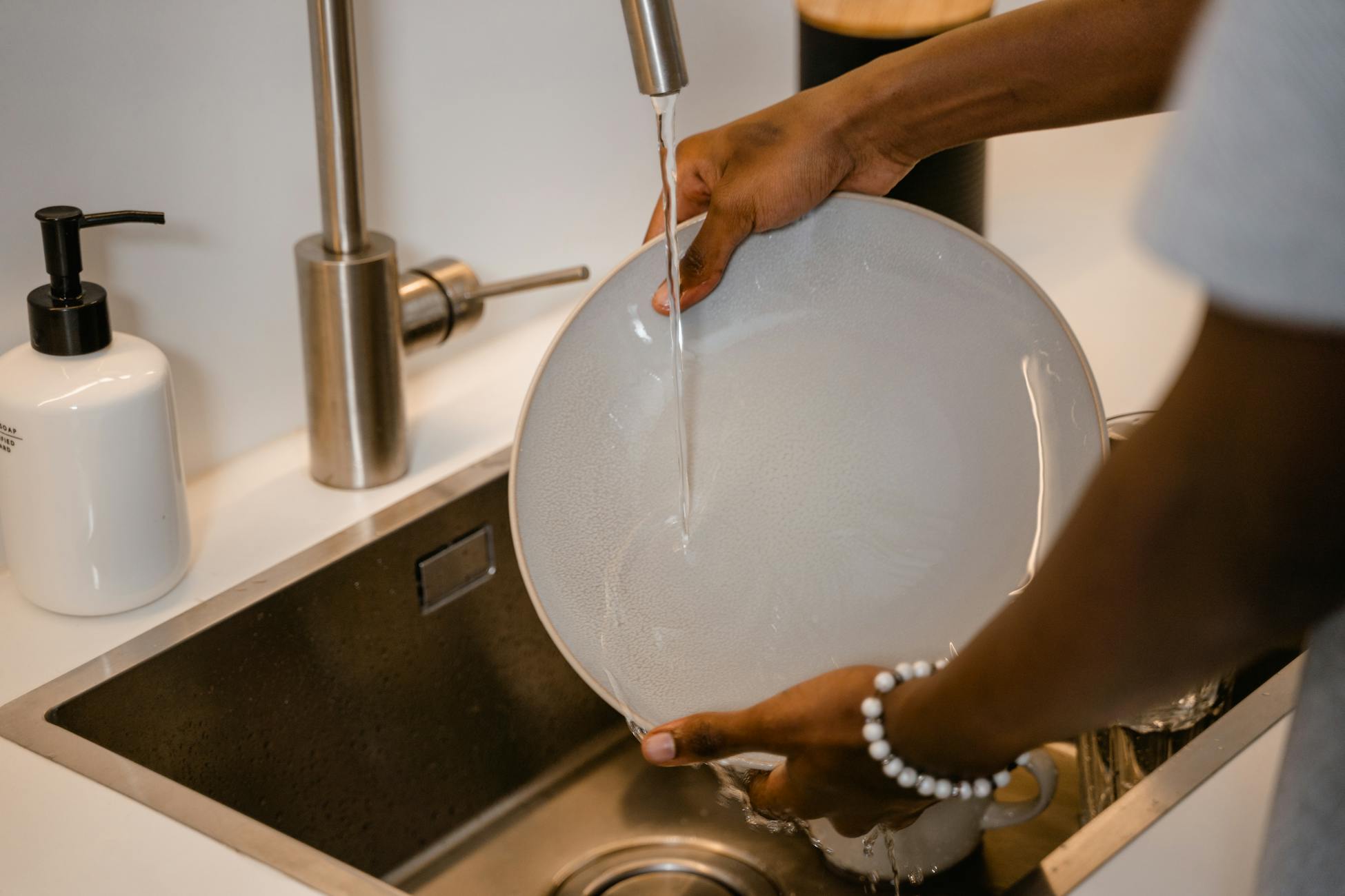 A close-up view of a person washing a plate in a modern kitchen sink with water running from the faucet.