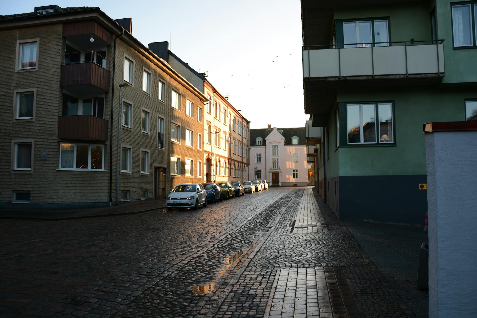 Cobblestone street with parked cars during sunset in a European city.