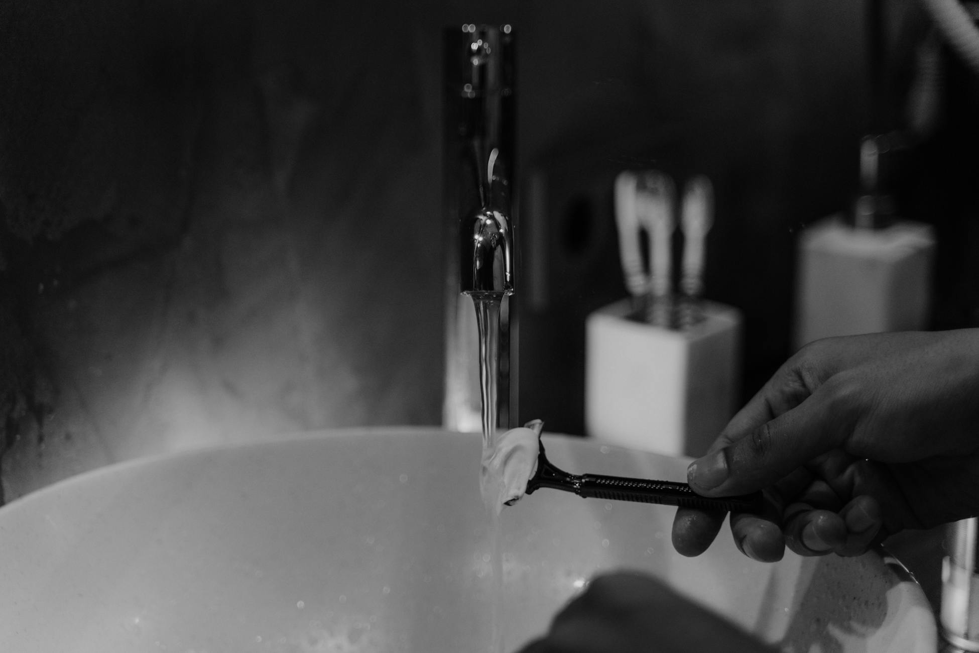 Close-up of a person shaving with water and foam in a contemporary bathroom sink.