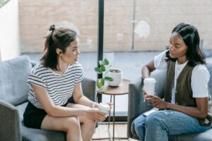 Two young women enjoying coffee and conversation indoors in a cozy setting.