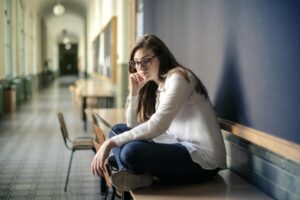 Thoughtful woman sitting alone in a school hallway contemplating problems.