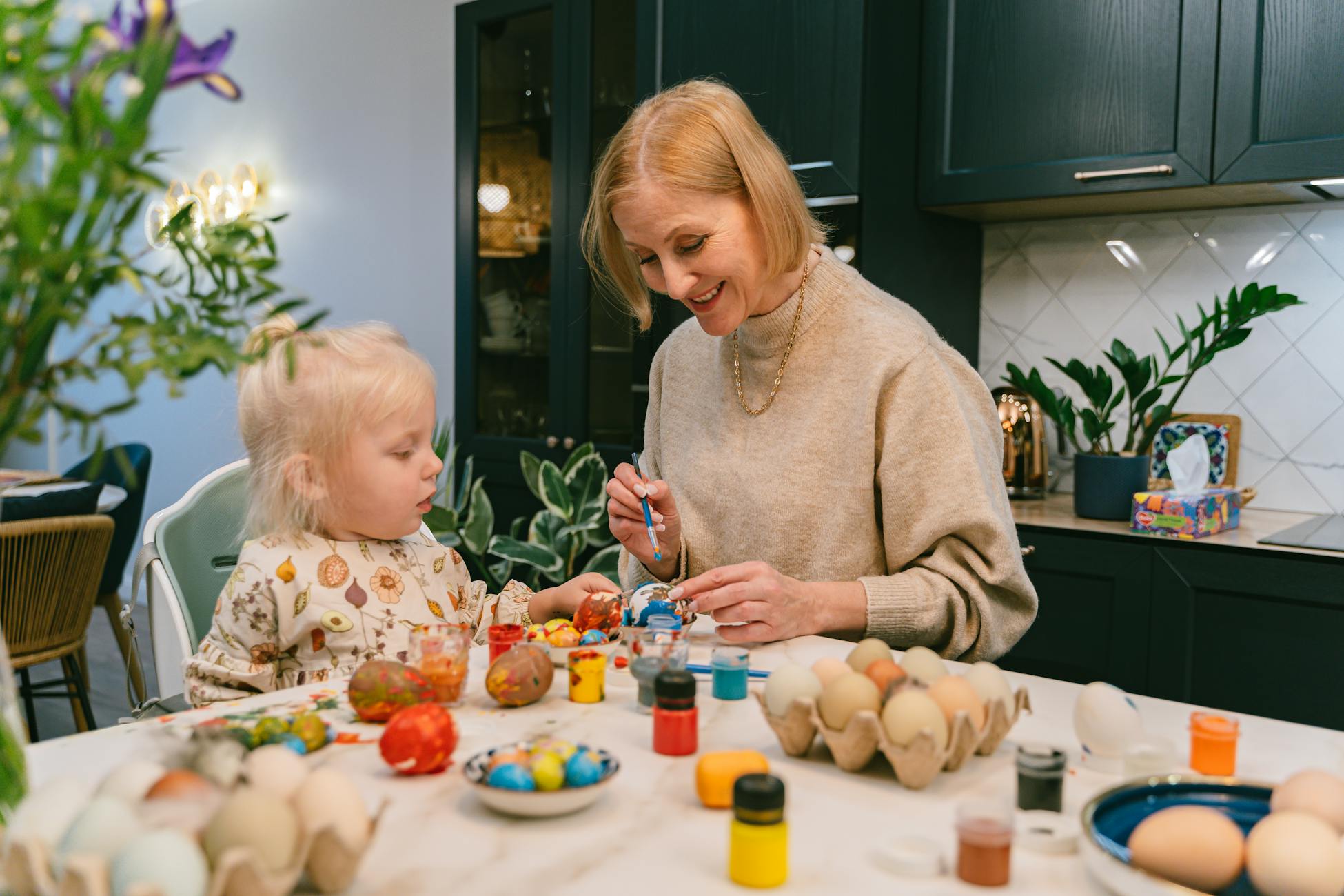 A grandmother and child enjoy painting Easter eggs together indoors, fostering creativity and bonding.