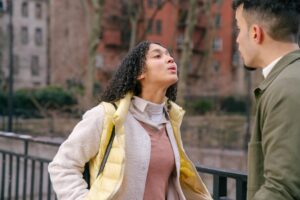 Hispanic female with black curly hair in casual clothes standing and having fight with boyfriend on street in daylight