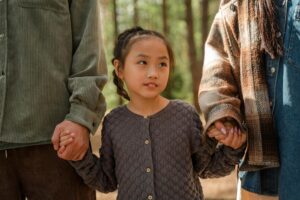 An adorable Asian girl holding hands with adults in a forest setting, expressing warmth and family love.