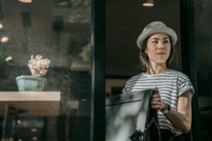 Asian woman carrying a chair indoors, wearing a hat and striped shirt. Modern and stylish setting.