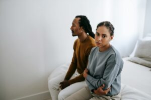 Frustrated thoughtful African American couple in casual wear sitting close on soft bed after quarrel