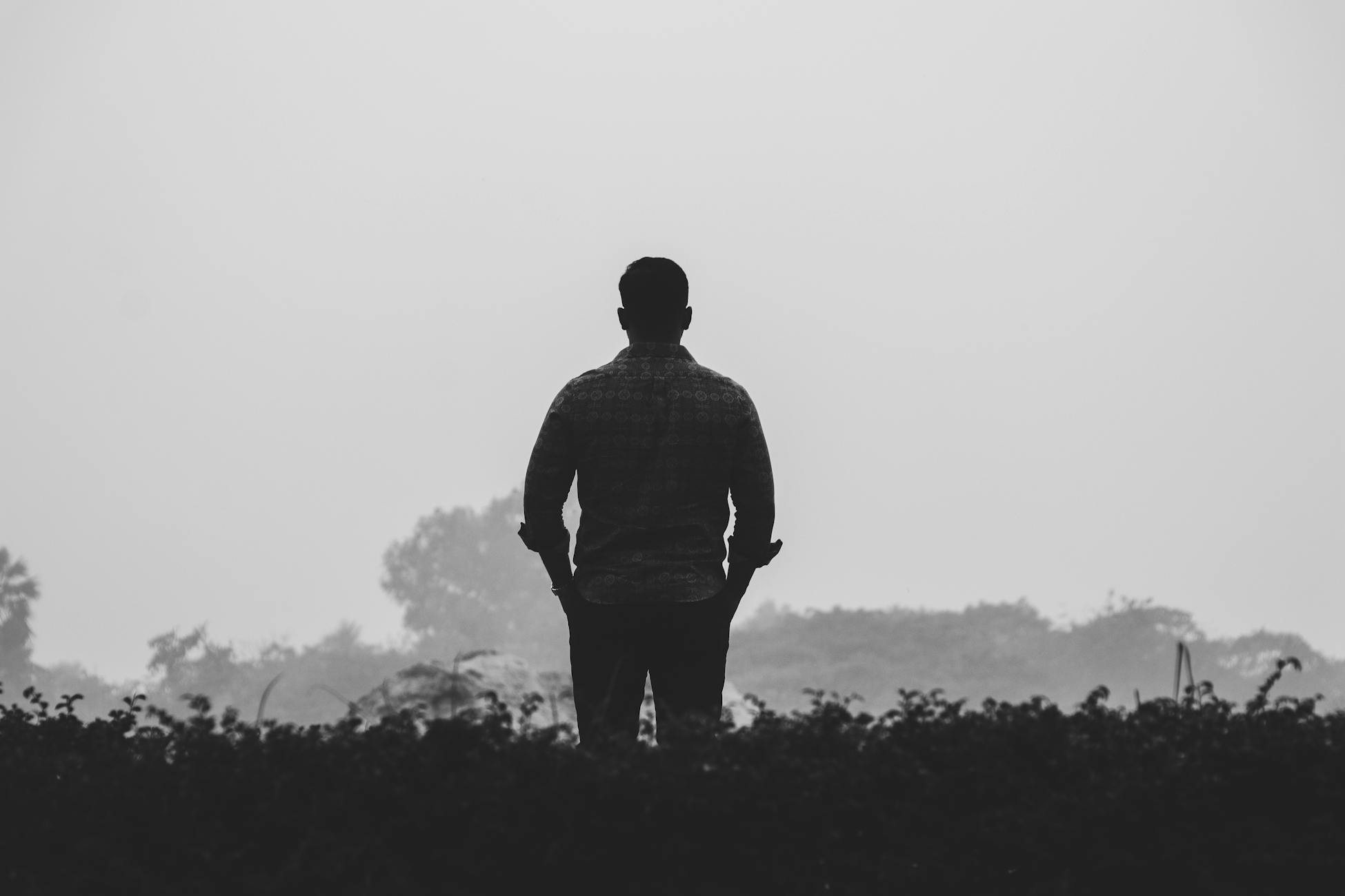 Silhouette of a man standing outdoors in a foggy, tranquil landscape.