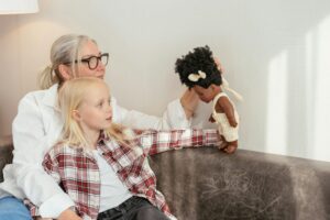 Grandmother and granddaughter enjoy quality time, playing with a doll on the sofa.