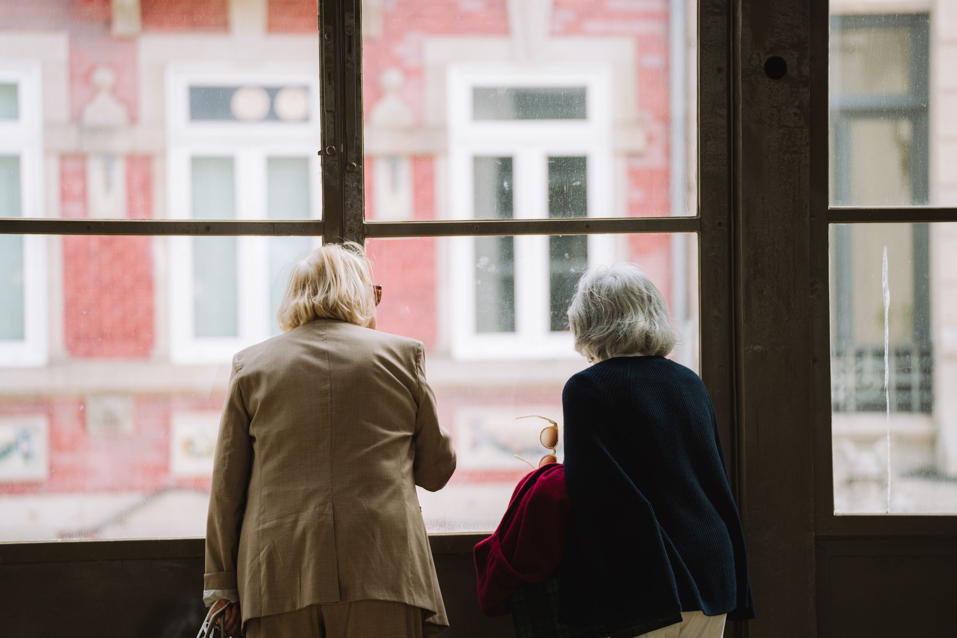 Two elderly women with gray hair look out of a window at a city scene, capturing a serene moment.