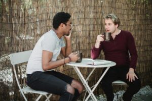 Two men enjoying a casual conversation over coffee outdoors with a rustic background.