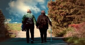 An older couple walking together along a tree-lined path, holding hands.