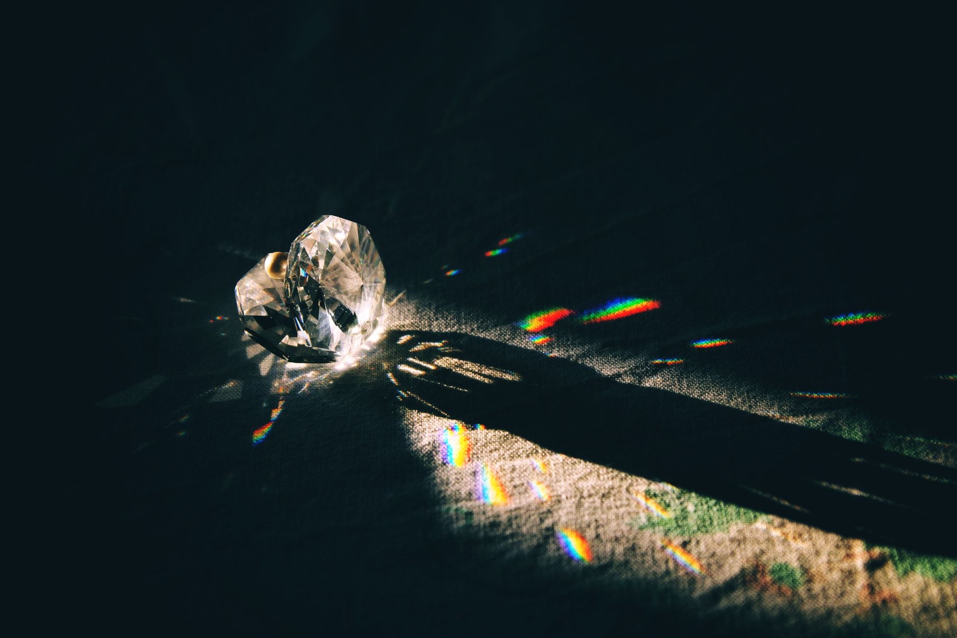 A diamond-shaped crystal casting rainbow reflections on a surface with dramatic lighting.