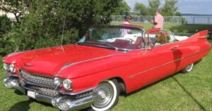 A classic red 1959 Cadillac convertible with tail fins and whitewall tyres parked on grass