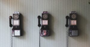 A row of three vintage black rotary wall telephones mounted on pale striped wallpaper