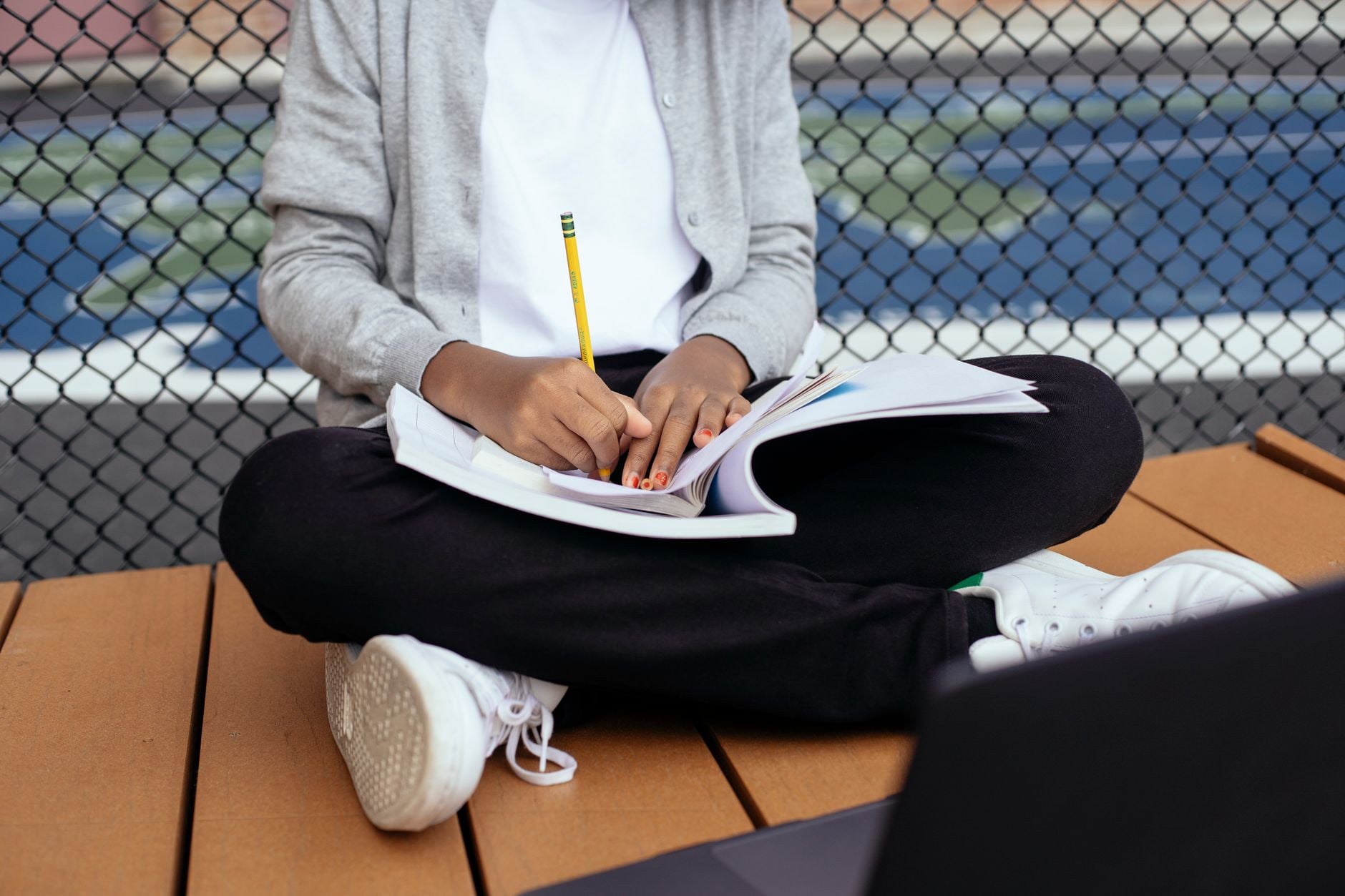 Crop unrecognizable schoolkid sitting with crossed legs and writing notes in copybook while studying with laptop
