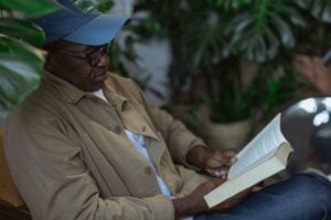 Senior man reading a book while relaxing indoors surrounded by plants