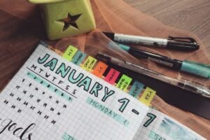 A detailed planner with goals and colorful tabs on a wooden desk with pens