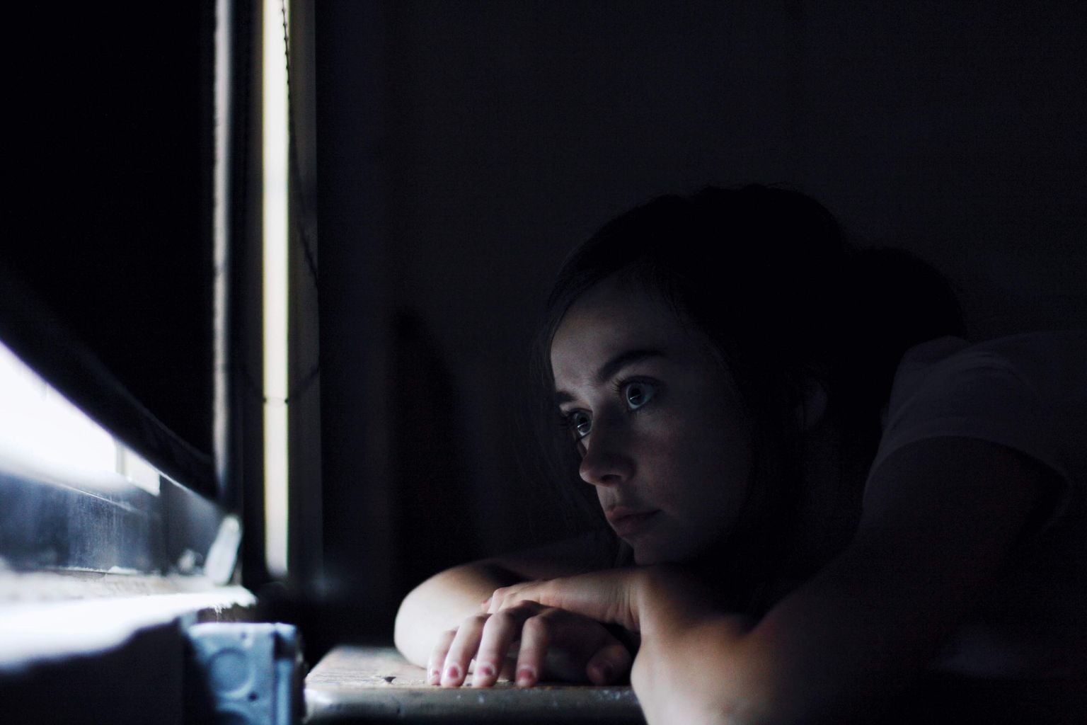 A person sitting alone in quiet thought by a window.
